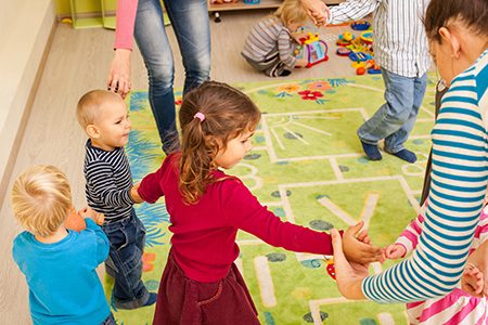 Group of little children dancing holding hands and enthusiastically watching the boy, who laughs with joy